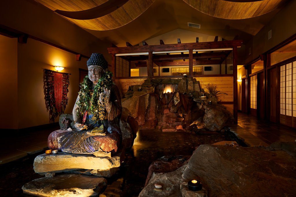 20240221-gritchelle-fallesgon-vco-juniper-preserve-winter-lifestyle-3390-medium (1) A serene Buddha statue adorned with a lei sits beside a small indoor waterfall in Central Oregon.