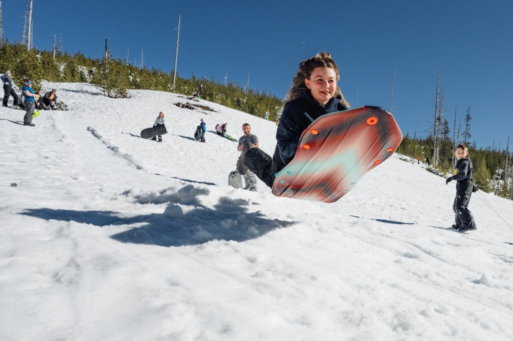 wanoga large-medium (2) A young girl jumps into the air while holding a colorful sled on snow in Central Oregon.