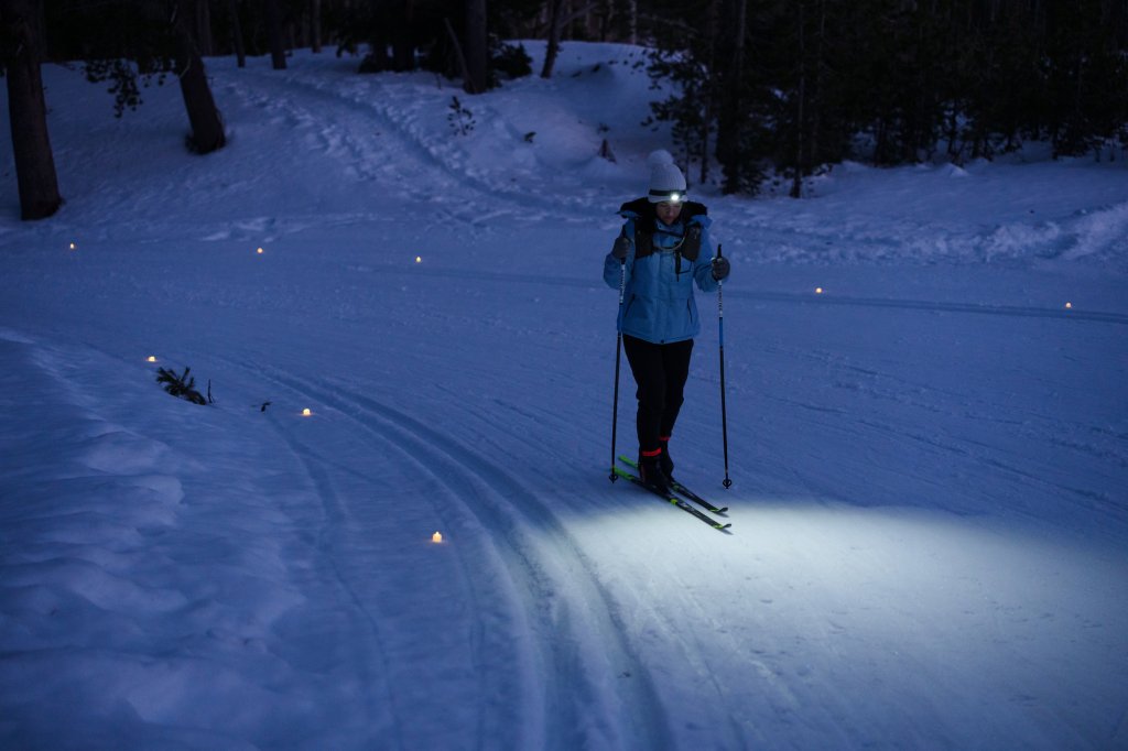 VCO_Cross_Country_Ski_Shoot_032422_VanWeelden-41-medium (1) A person cross-country skiing at night on a trail illuminated by small lights in Central Oregon.
