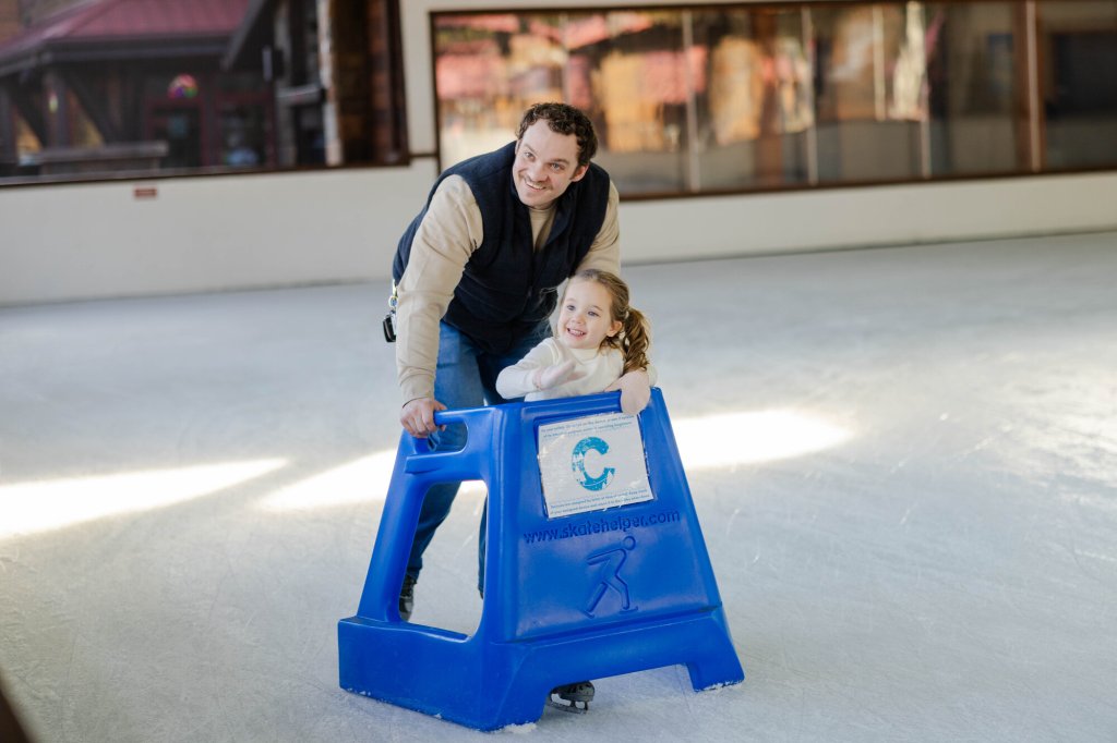photography by steve heinrichs-22-medium (1) A man helps a young girl learn to ice skate using a blue support frame in Central Oregon.