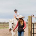 An image of a a woman guiding a person riding a horse from Sunriver Stables