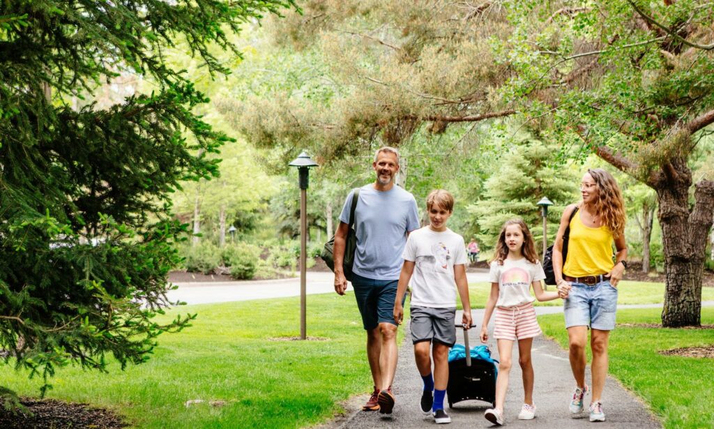 Family of four walks on paved path with luggage at Sunriver Resort