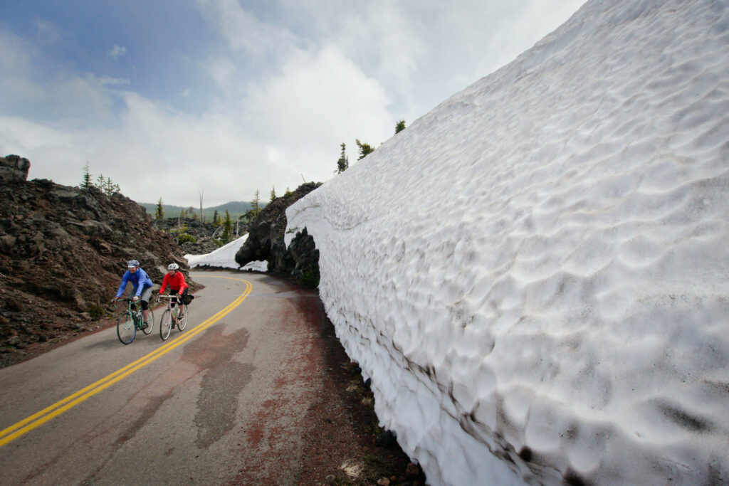 A pair of cyclists ride past a wall of snow along McKenzie Pass near Sisters, Oregon.