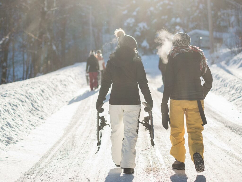 A pair of friends walk along a snow-covered road while holding snowshoes near Bend, Oregon.