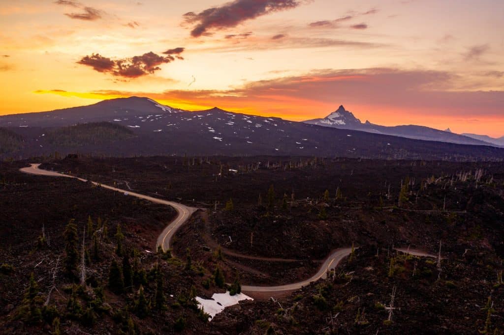 a winding road surrounded by lava rock, trees, and the Mt Washington in the background