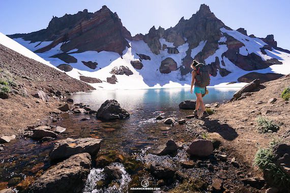A woman walks into No Name Lake in front of Broken Top in the Cascade Range near Bend, Oregon.