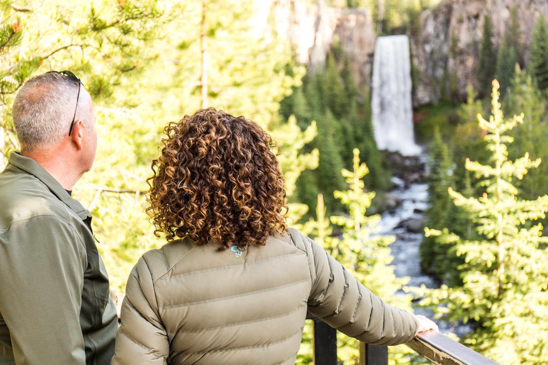 A couple admires a majestic waterfall in a lush forest setting in Central Oregon.