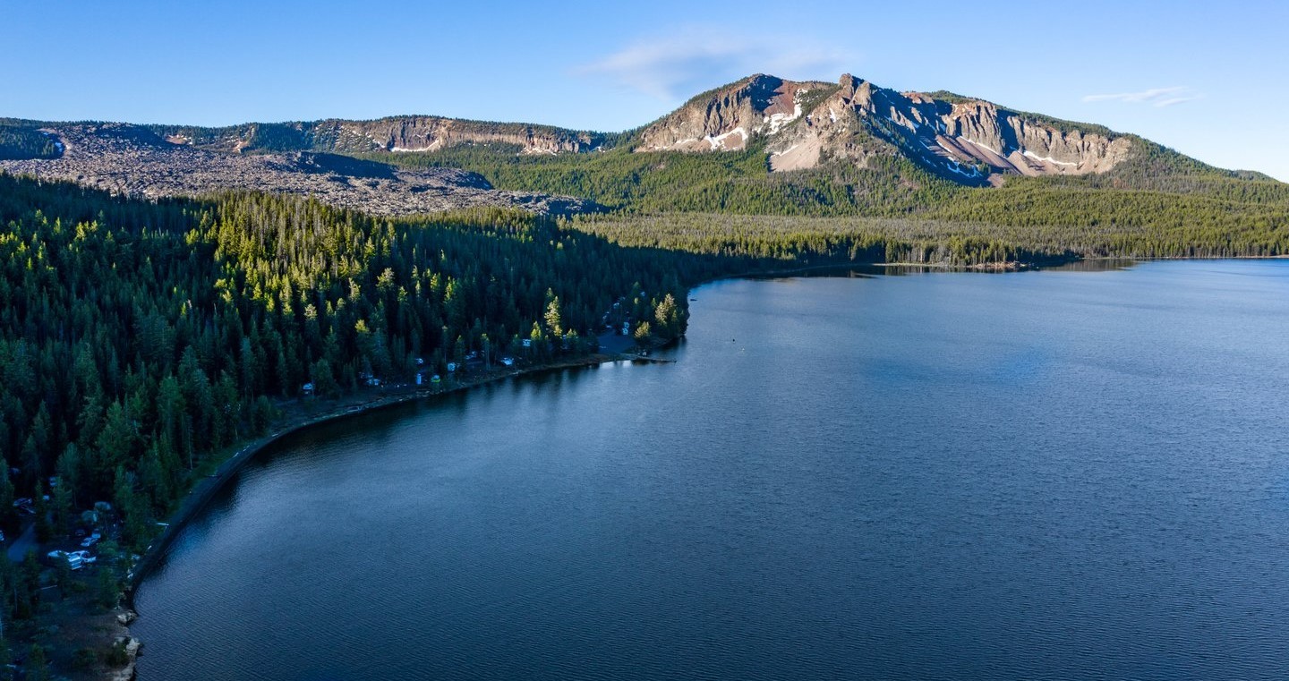 A serene lake surrounded by lush forest and majestic mountains under a clear blue sky in Central Oregon.