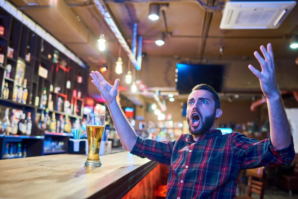 man with a beer cheering emotionally while watching a game at a brewery