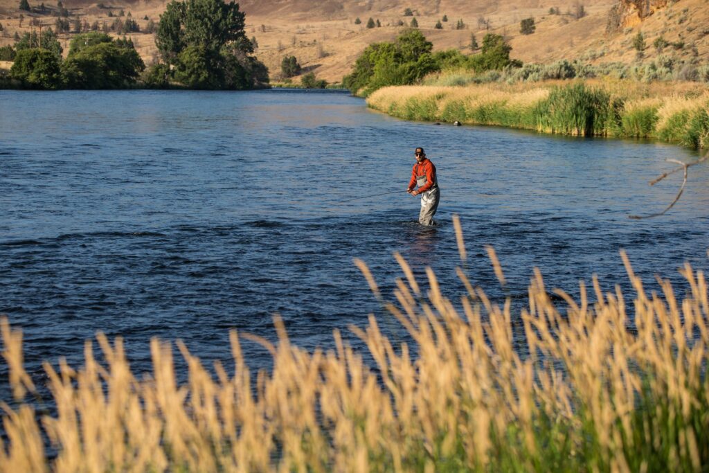 A man fishing in a serene river surrounded by nature in Central Oregon.