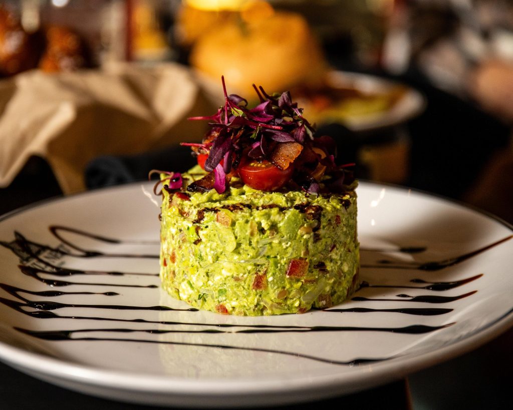 A vibrant green avocado mousse tower topped with microgreens and a cherry tomato in Central Oregon.