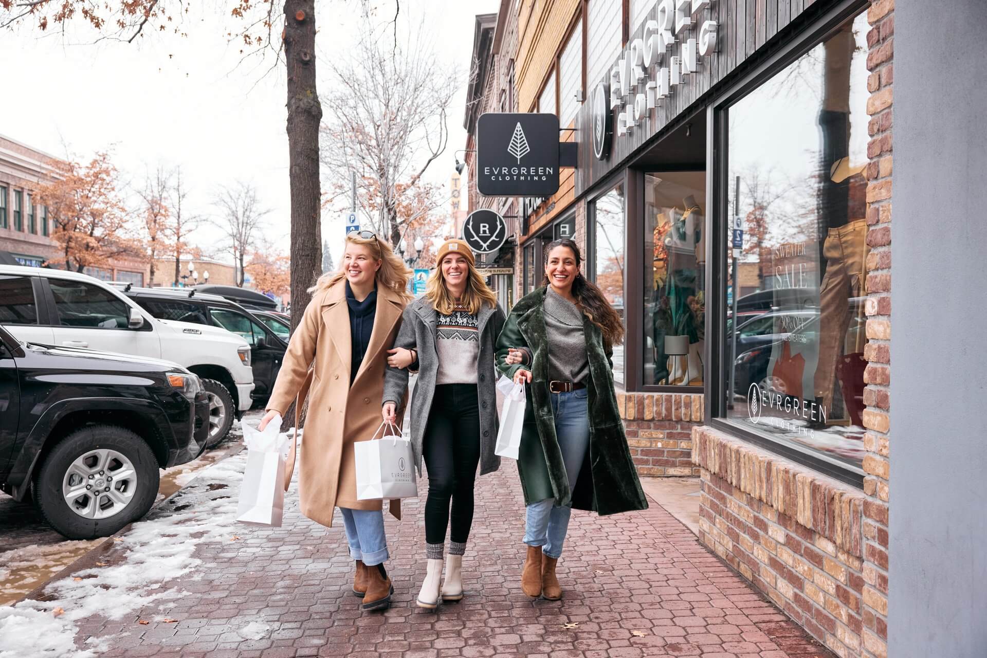 Three women walk down a snowy street, carrying shopping bags from a clothing store in Central Oregon.