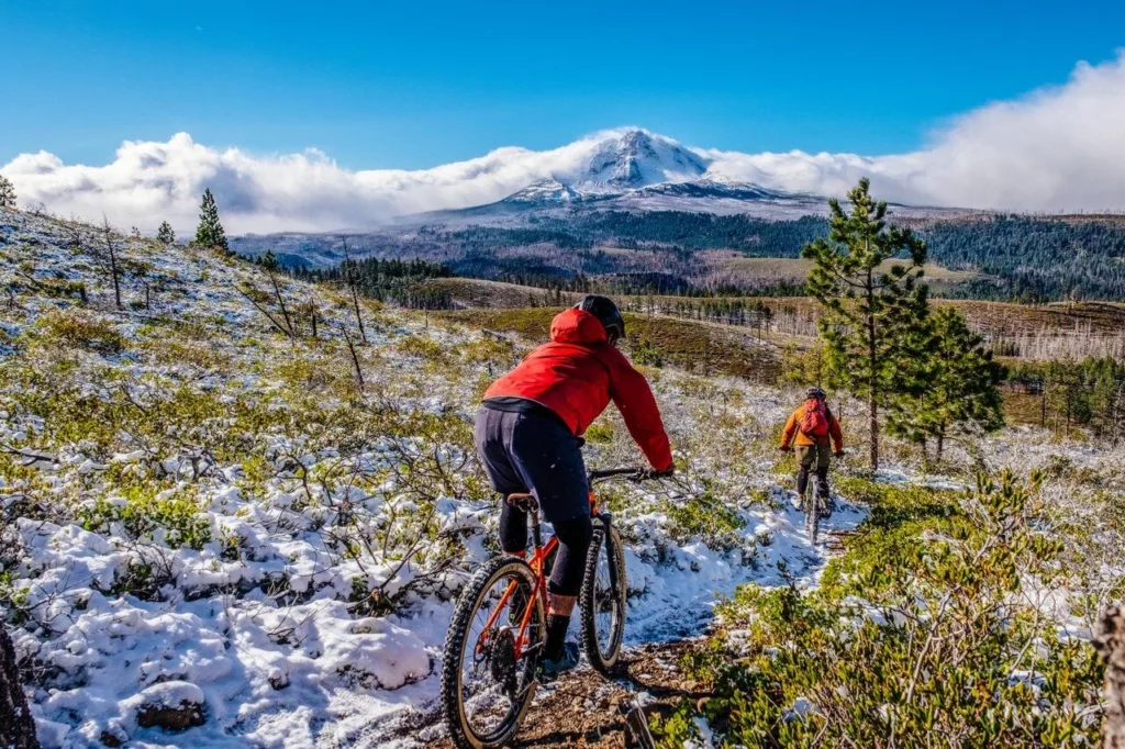 Two mountain bikers descend down a snowy trail 