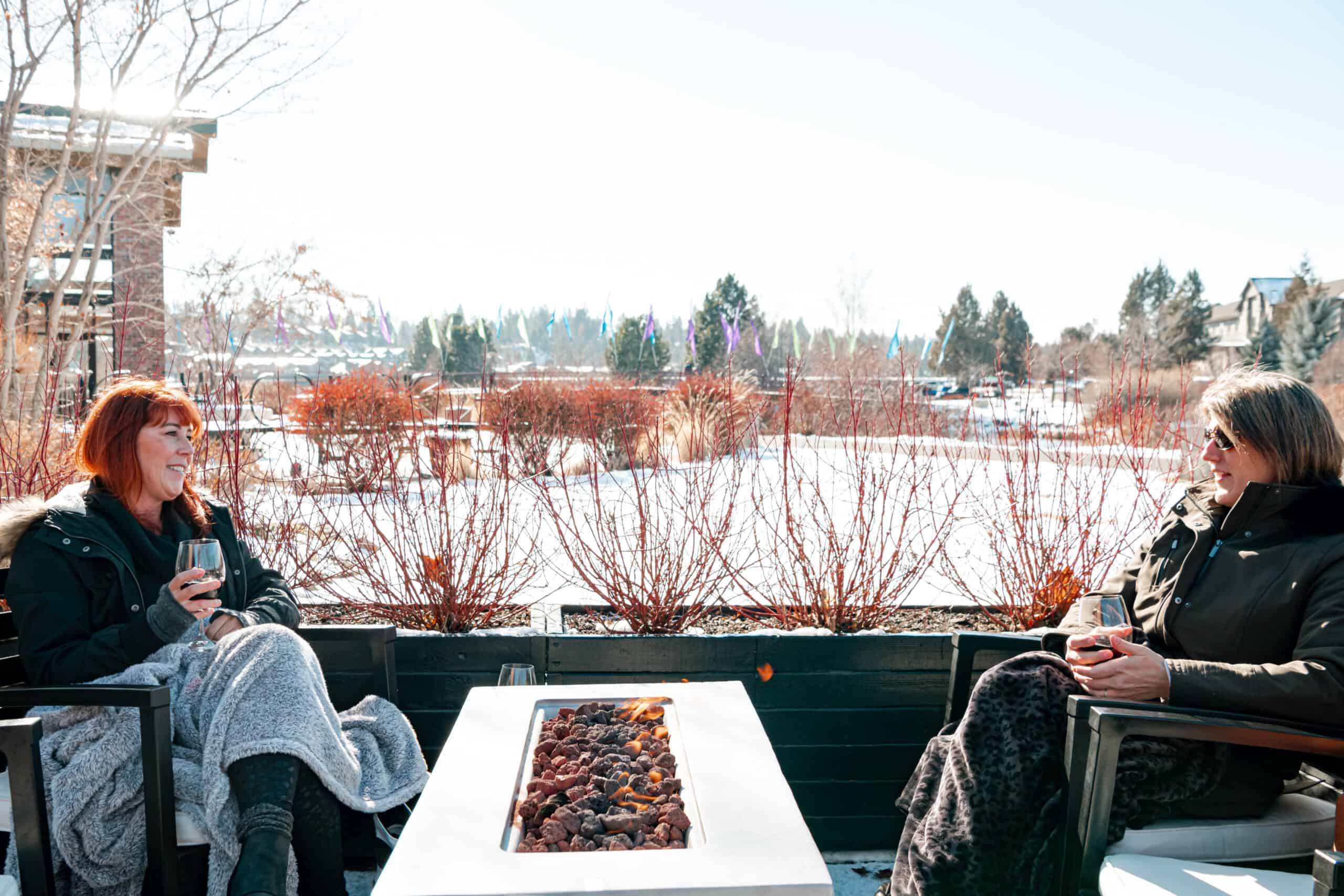 two ladies drinking wine outside in winter by a fire pit
