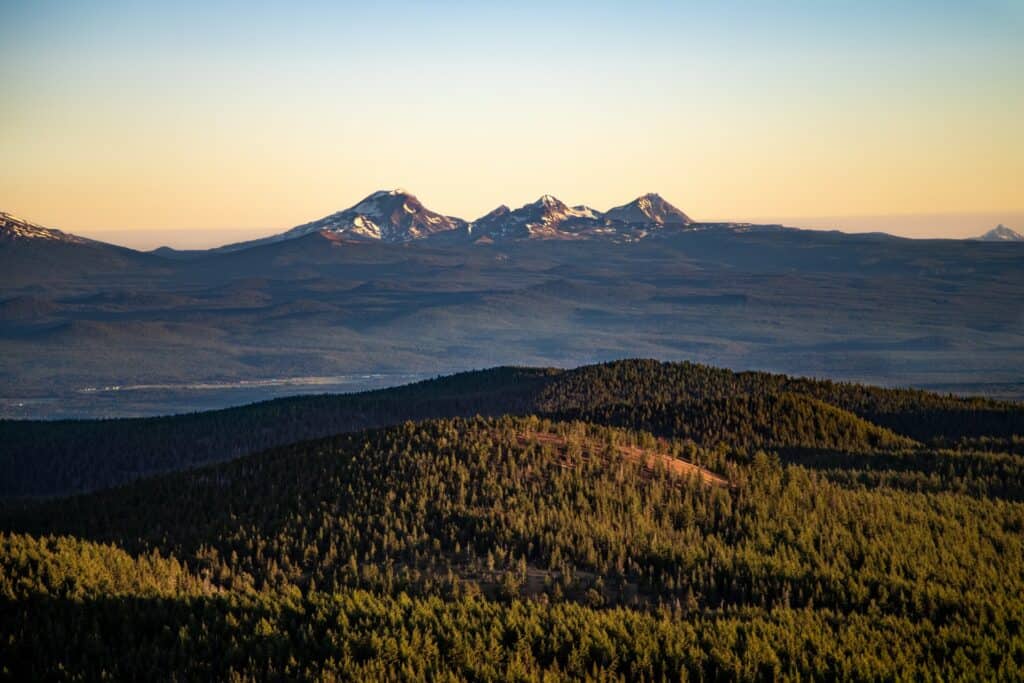 A breathtaking mountain landscape at sunset, featuring snow-capped peaks and lush forests in Central Oregon.