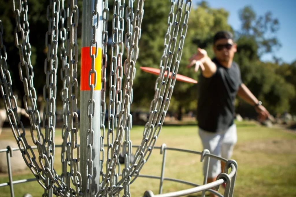 A person playing disc golf throws the disc into the basket.