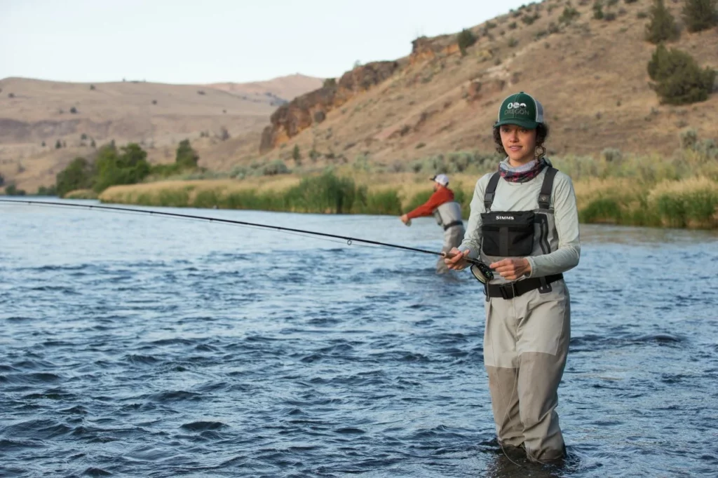 A woman wades through the river while fly fishing.