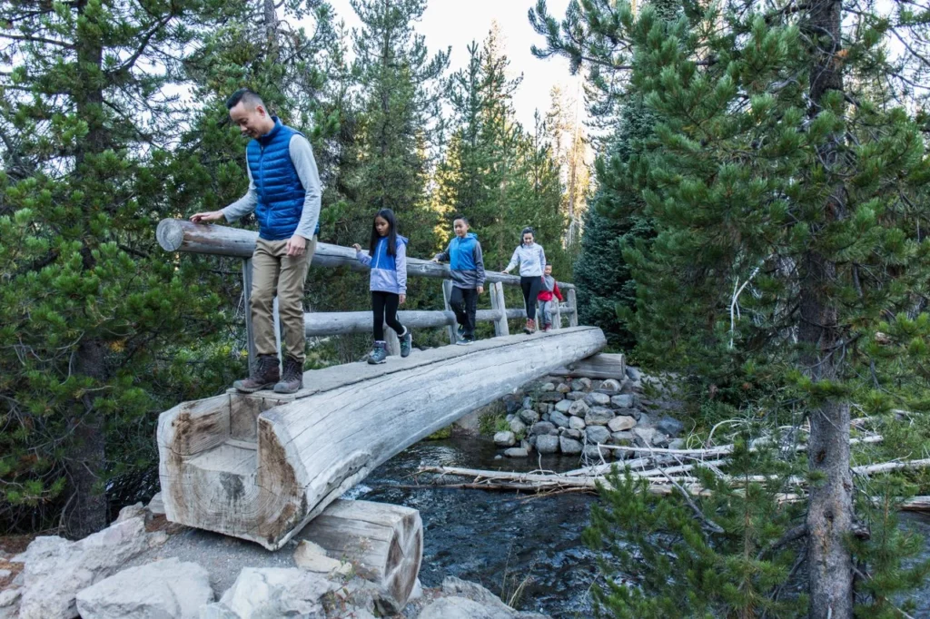 A family crosses a wooden bridge while hiking on the Green Lakes Trail.