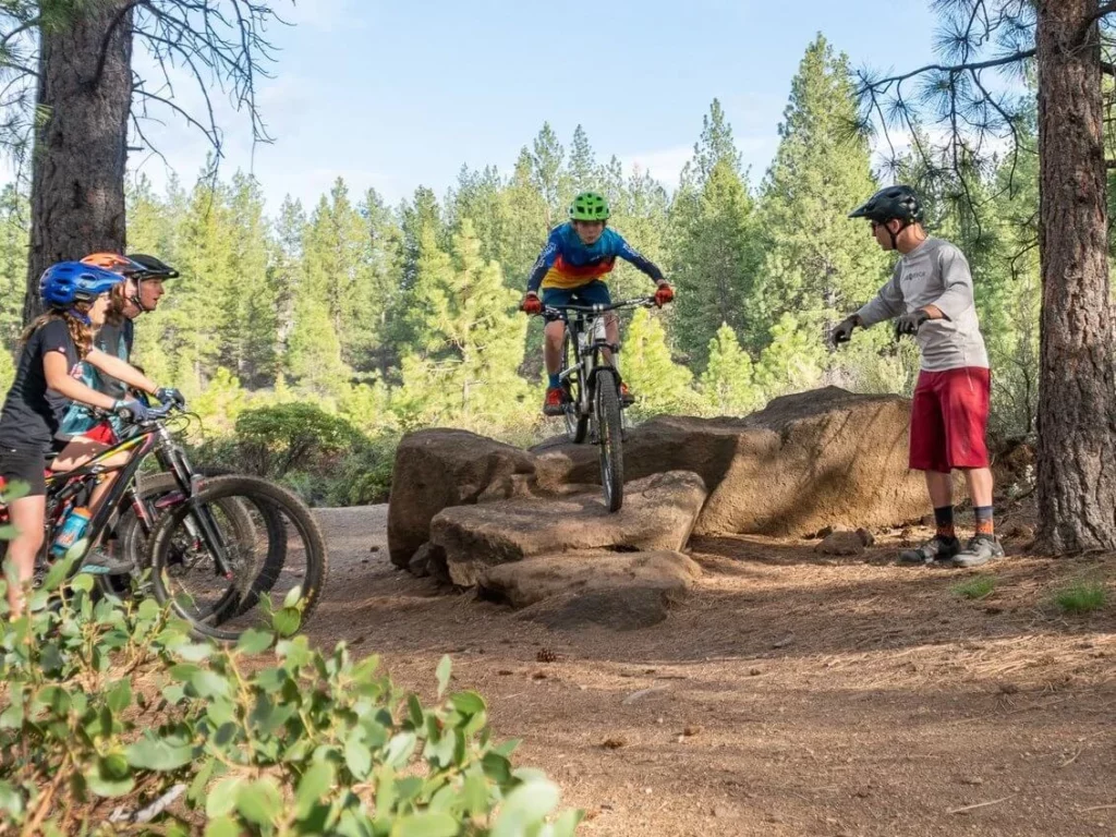 A mountain bike guide shows a biker how to go over a rock. 