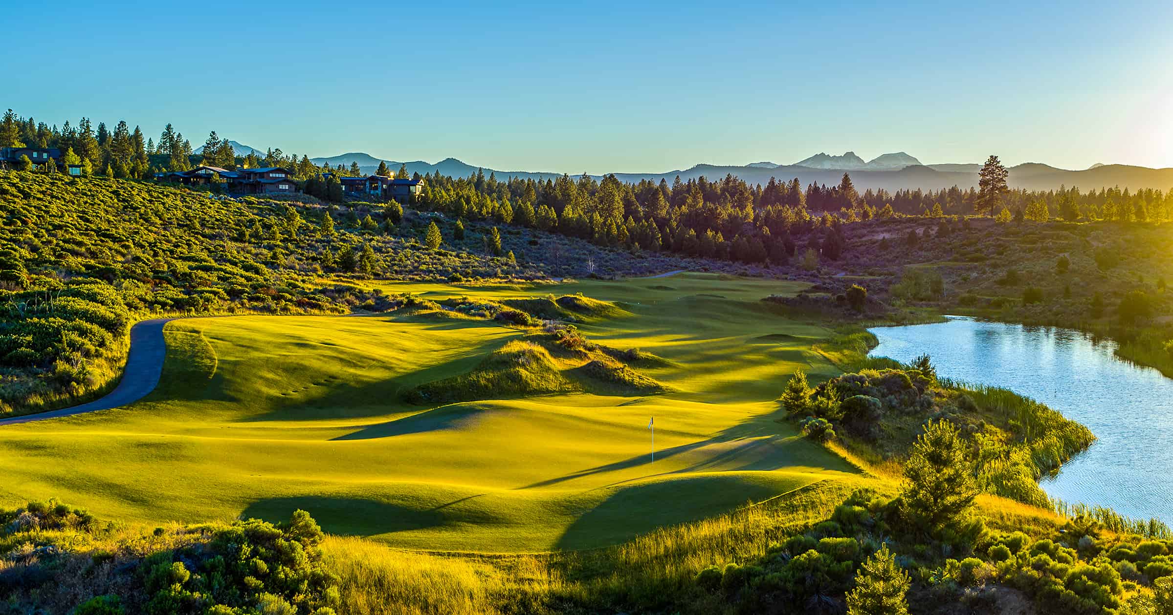 An aerial view of the lush golf green and a body of water surrounded by forest at Tetherow Resort.