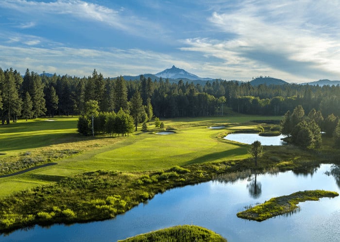 A serene golf course with lush green fairways, sparkling lakes, and a majestic mountain range in the distance in Central Oregon.
