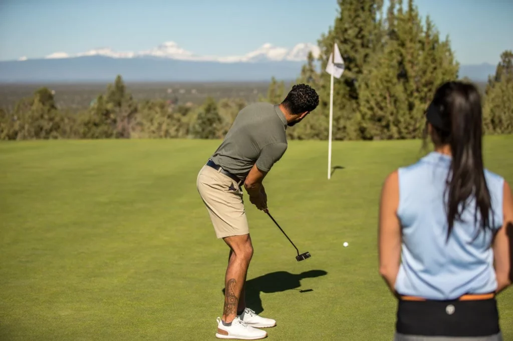 A golfer prepares to putt on a lush green golf course with a scenic mountain backdrop in Central Oregon.