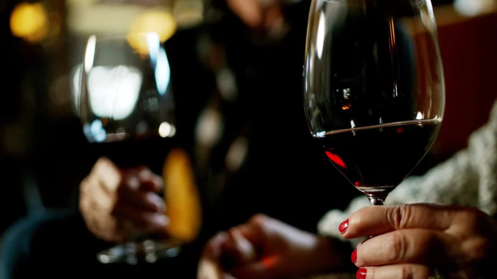 Two hands holding wine glasses, one with red wine, set against a blurred background in Central Oregon.