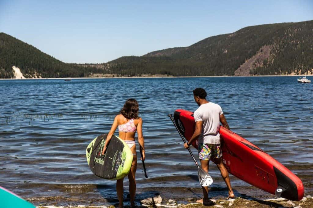 Two people walk out to SUP on a lake. 