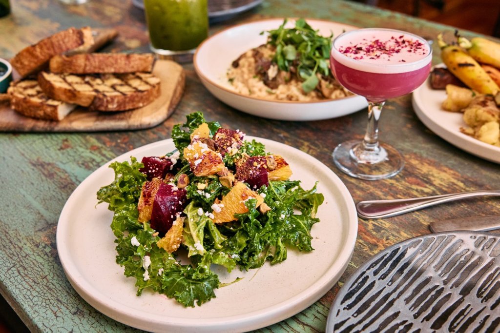 A vibrant table setting featuring a pink cocktail, grilled vegetables, and a colorful salad with beets and kale in Central Oregon.