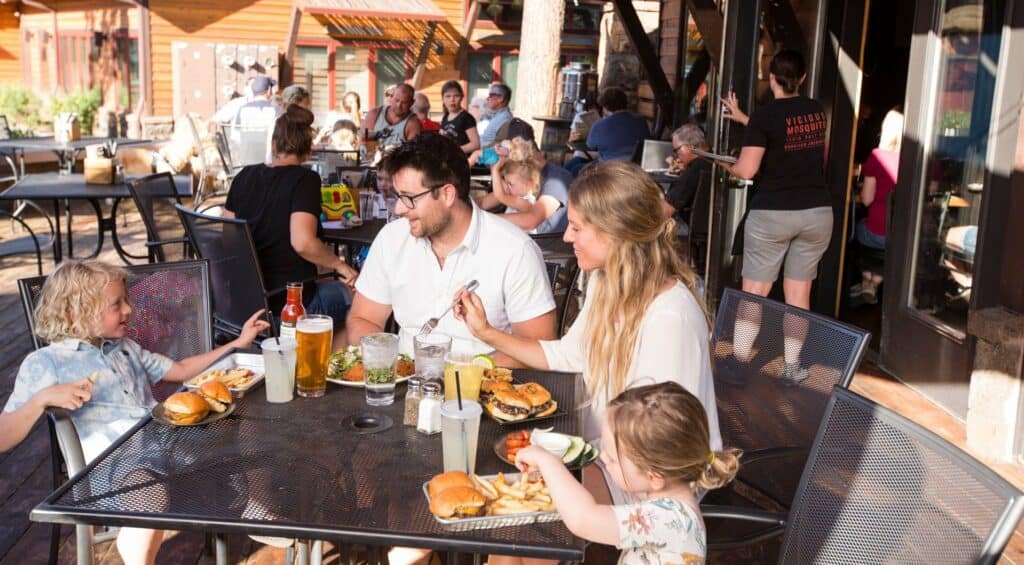 A lively outdoor restaurant scene with families enjoying meals and drinks in Central Oregon.