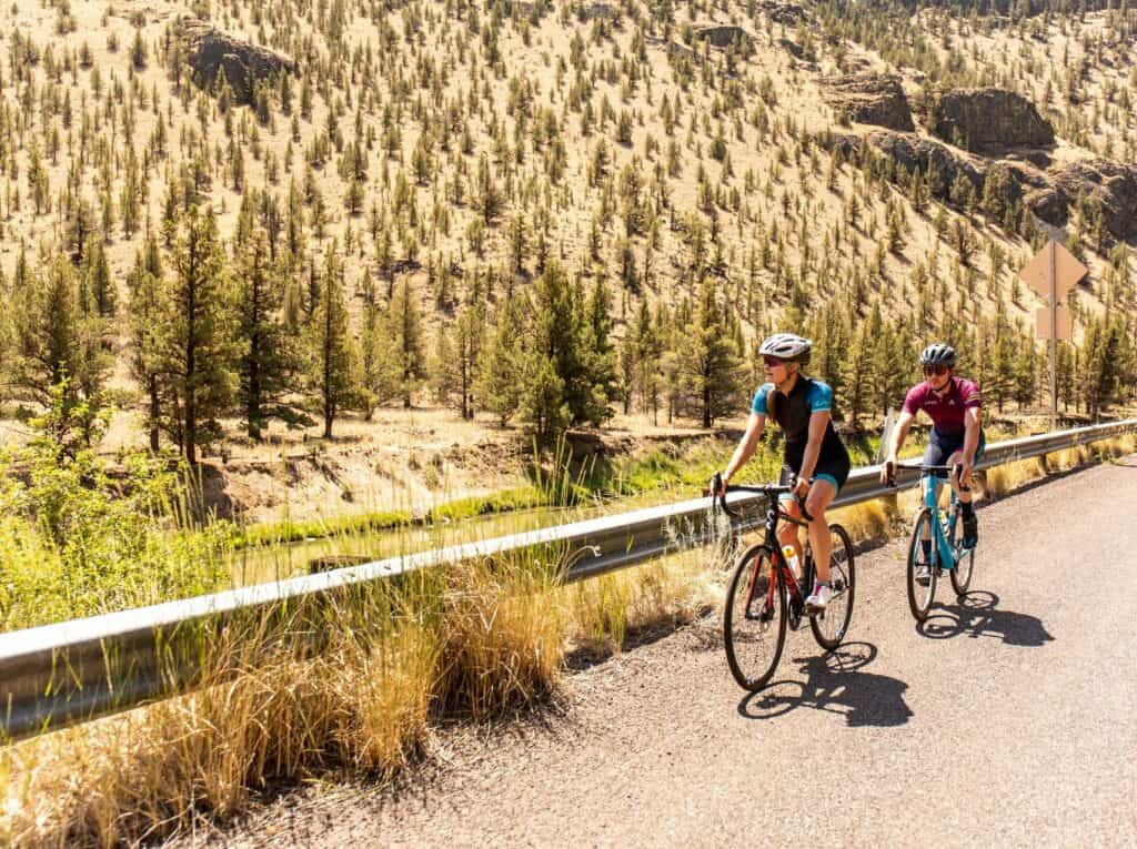 Two cyclists ride along a scenic road surrounded by nature in Central Oregon.