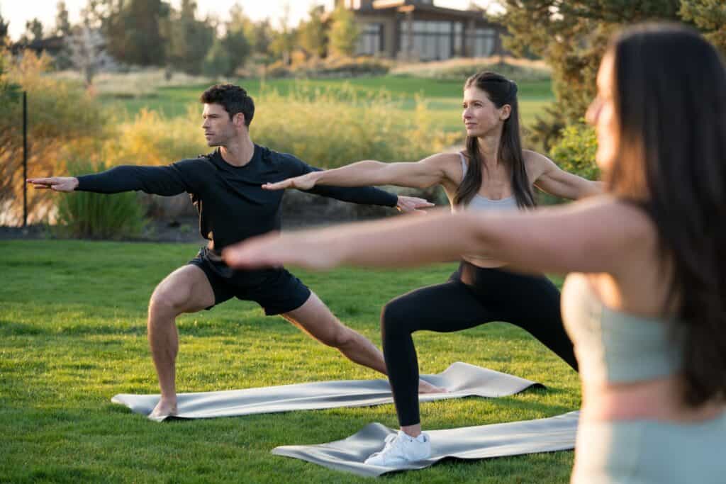 Three individuals practicing yoga in a serene outdoor setting, stretching and balancing on mats in Central Oregon.