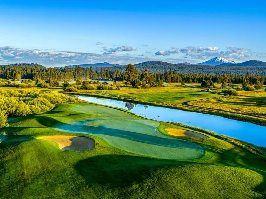 A serene golf course with lush green fairways, a winding river, and majestic mountains in the distance in Central Oregon.
