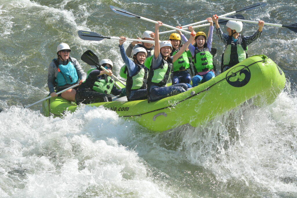 A group of people enjoying a thrilling whitewater rafting adventure, navigating through rough rapids in a bright green inflatable raft in Central Oregon.