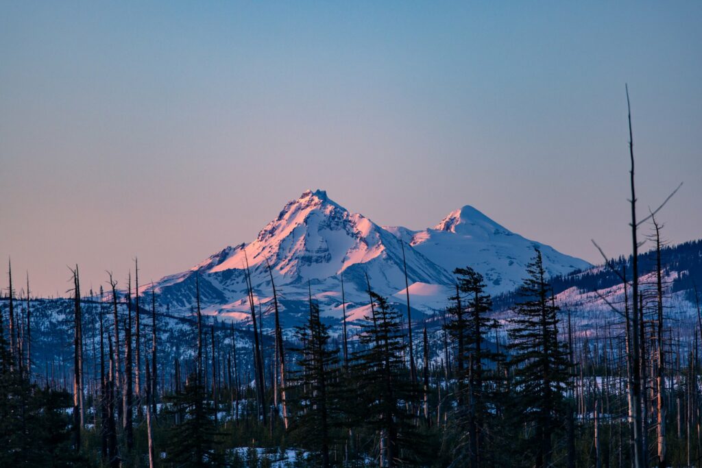 A majestic mountain range at sunset, with snow-capped peaks and a forest of tall trees in Central Oregon.