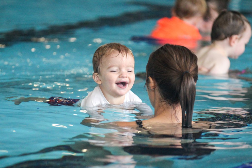 A happy toddler smiling at an adult while swimming in a pool in Central Oregon.