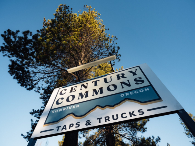 A sign for Century Commons in Sunriver, Oregon, featuring a mountain range and the words 'Taps & Trucks' in Central Oregon.