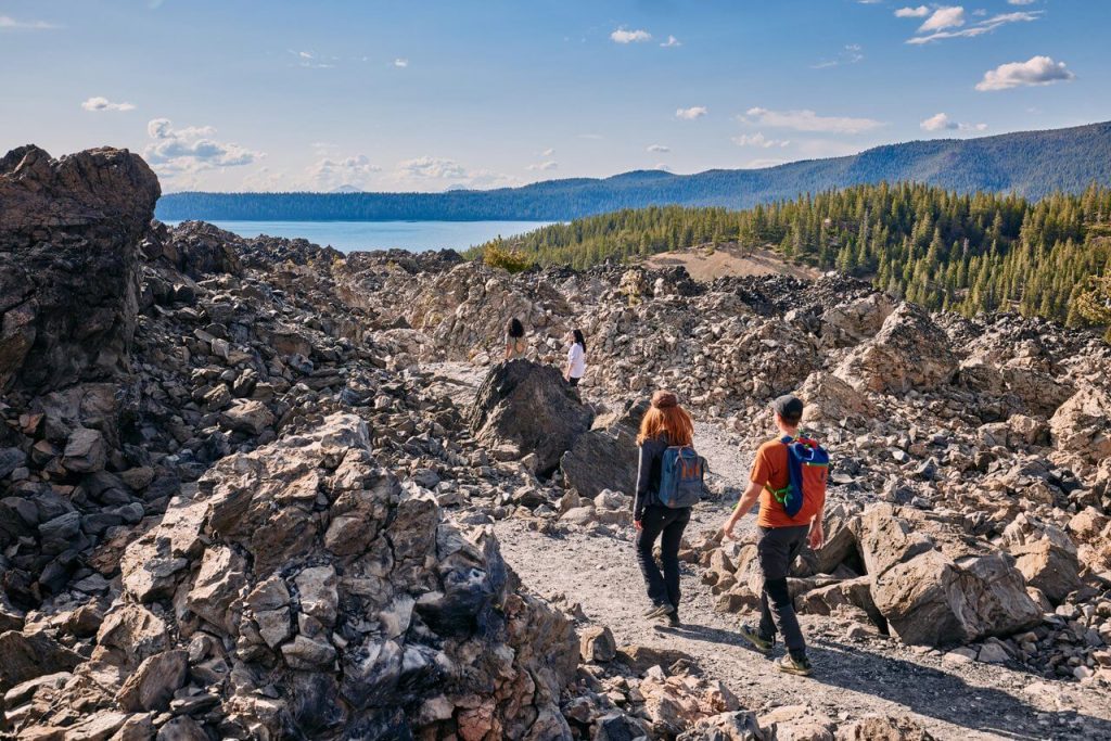 Hikers explore a rocky terrain with a scenic lake and mountains in the distance in Central Oregon.