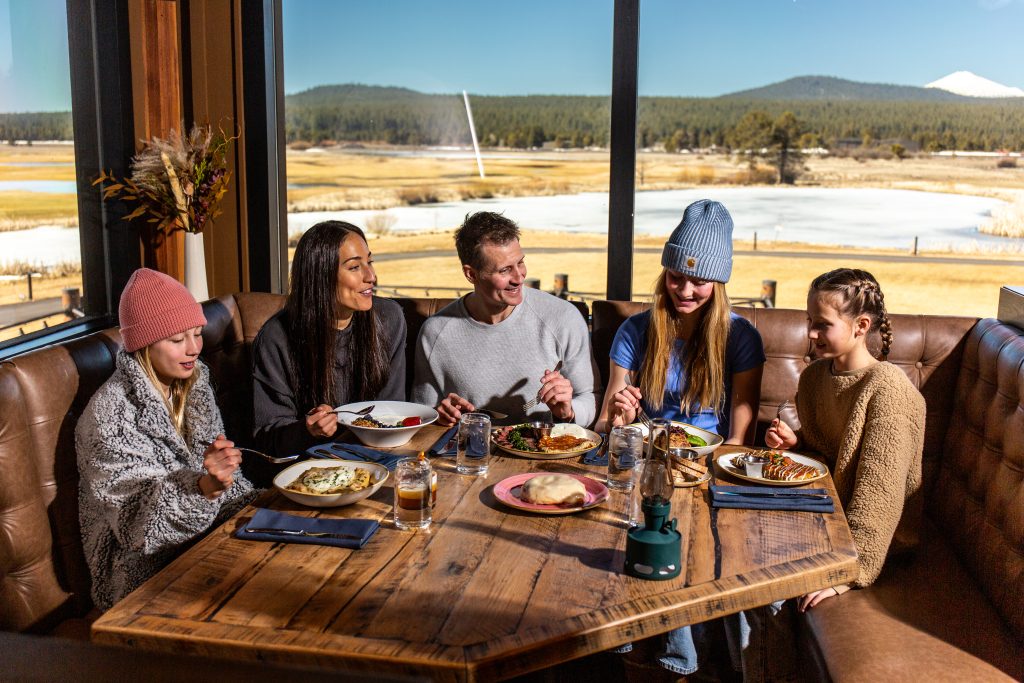 A group of friends enjoying a meal together in a cozy restaurant with a stunning outdoor view in Central Oregon.