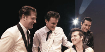 Four men in suits and cowboy hats, laughing and hugging on stage in Central Oregon.
