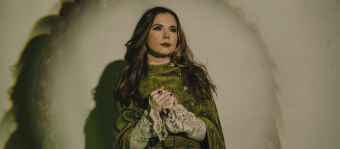 A woman in a green cloak with lace sleeves stands in a dramatic setting in Central Oregon.