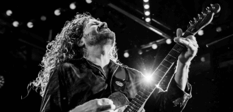 A musician with long, curly hair passionately playing an electric guitar on stage in Central Oregon.