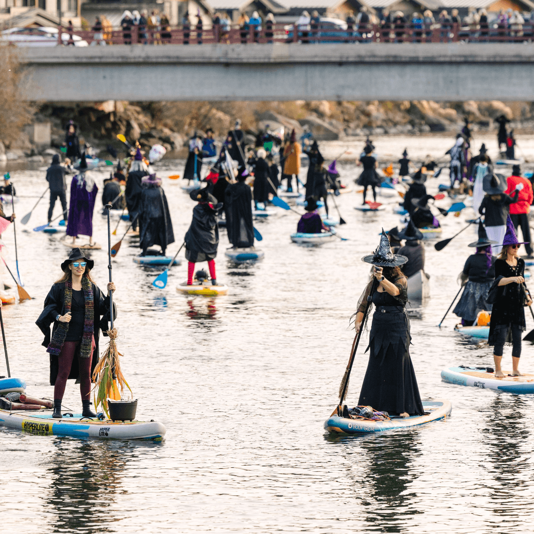 A large group of people dressed as witches paddle on paddleboards in a river during a Halloween event in Central Oregon.