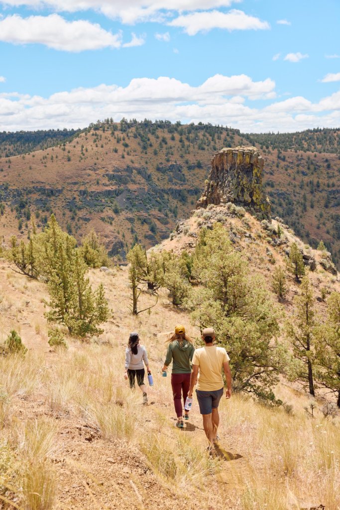 Three hikers explore a rugged desert landscape, surrounded by sparse vegetation and towering rock formations in Central Oregon.