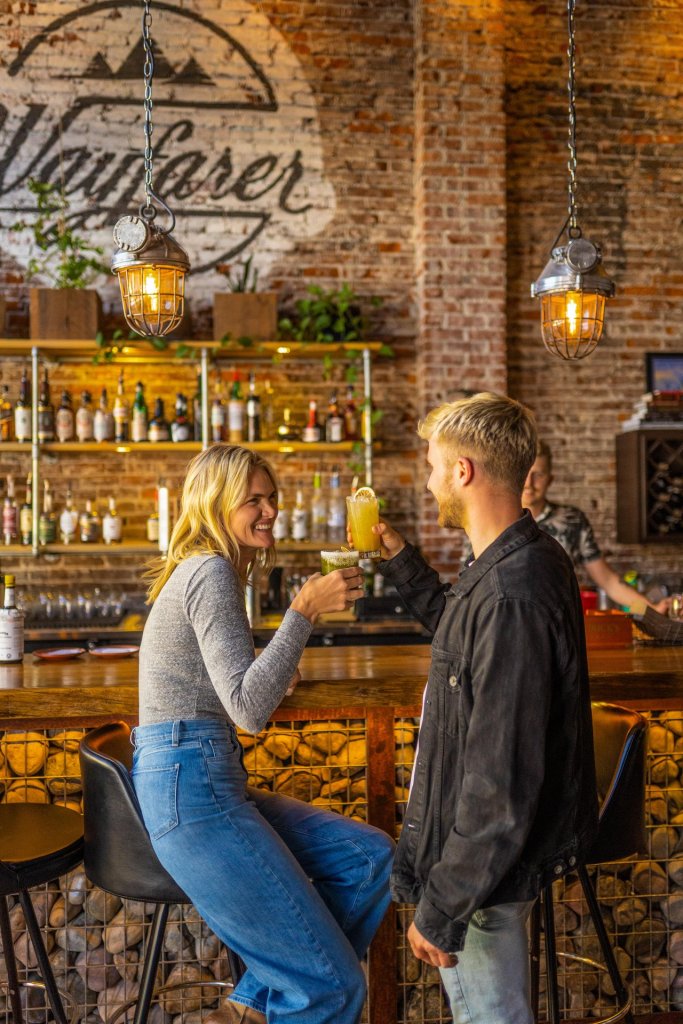 A cheerful woman and man share a toast at a cozy bar with rustic decor in Central Oregon.