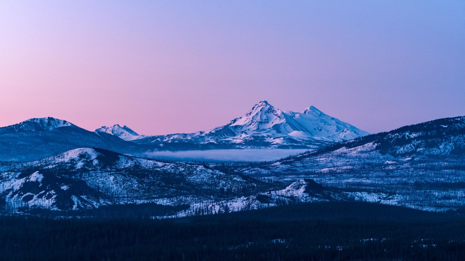 A breathtaking mountain range at twilight, with snow-capped peaks and a pink sky in Central Oregon.