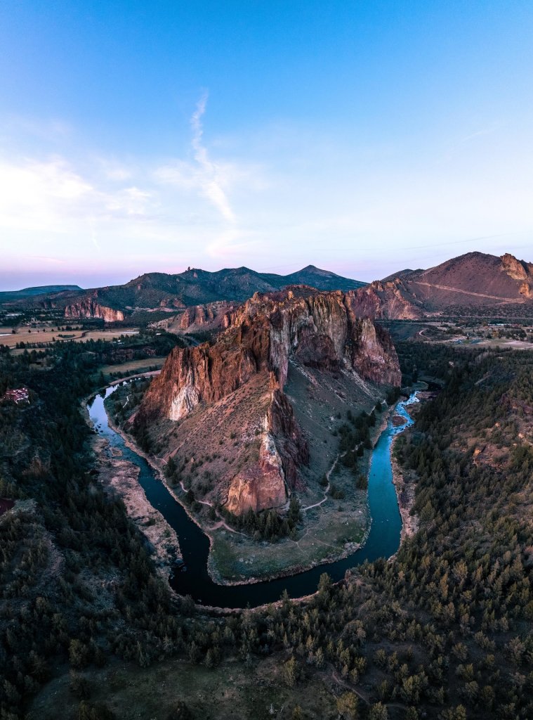 A winding river meanders through a lush valley, surrounded by towering cliffs and dense forests in Central Oregon.