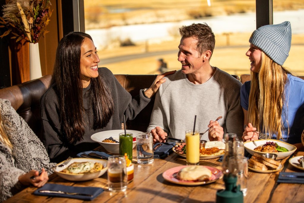 A group of friends enjoying a meal together at a cozy restaurant with a scenic view in Central Oregon.
