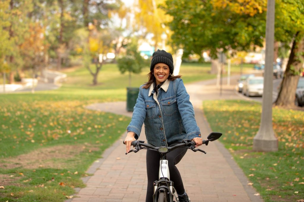A woman rides her bike along a tree-lined path, smiling and enjoying the autumn weather in Central Oregon.