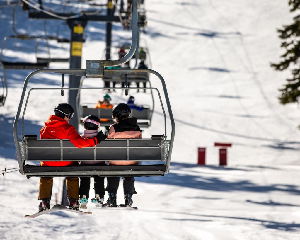 A family of four, dressed in winter sports gear, riding a ski lift on a snowy mountain in Central Oregon.